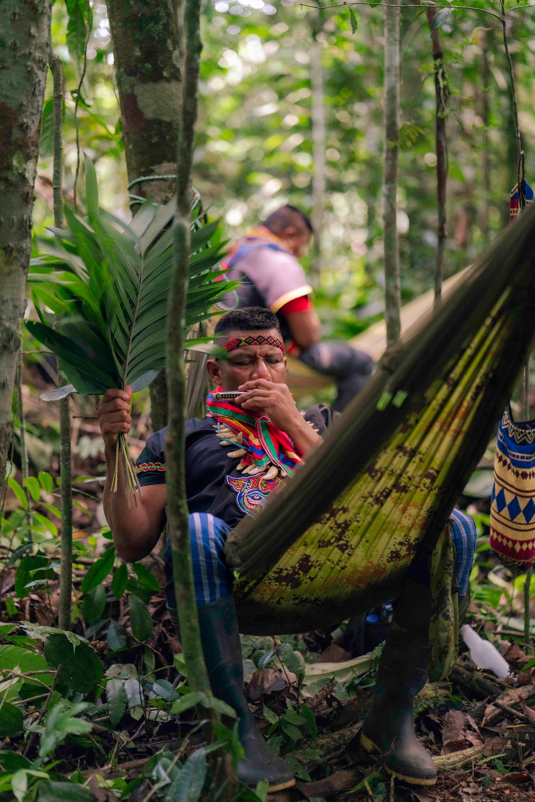 Kofán elder in traditional dress holding palm fronds in the forest